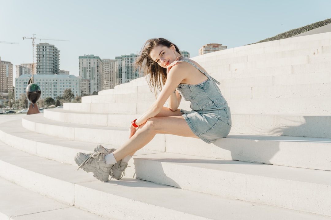 young-woman-in-denim-dress-sitting-on-white-steps-fo-ajhieq9a